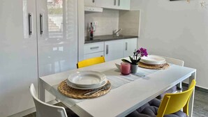 Cuina moderna amb armaris blancs, una taula de dinar preparada amb plats, una petita planta en test i una prestatgeria de paret amb objectes decoratius.