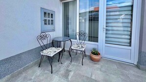 Un pati amb dues cadires metàl·liques, una taula petita, una planta en test i una porta corredissa de vidre.
