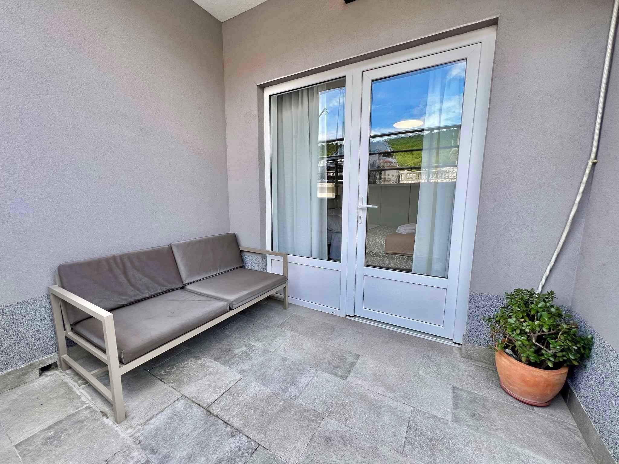 Ein Balkon mit einer grauen Couch, einer Schiebetür aus Glas und einem Blumentopf.