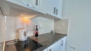 Una cuina moderna amb armaris blancs, un fogó integrat, una papereta i una ampolla de vi.