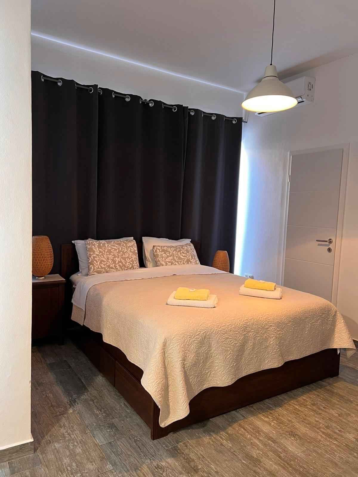 Ein Schlafzimmer mit Bett, dunklen Vorhängen, einer Nachttischlampe und einer Tür.