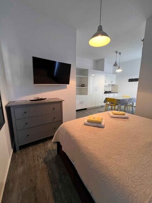 A modern bedroom with a bed, a TV, a dresser, and a kitchenette in the background. - Studio with air conditioning and sea view (Crikvenica)