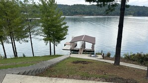 A gazebo with a roof and steps leading to a dock by a lake, surrounded by trees and a grassy area. - SPACIOUS Lakeside Home in the perfect LOCATION near all the action! (LaFollette)
