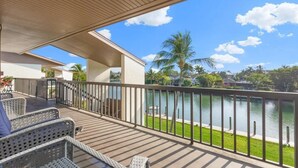 A covered outdoor deck with wicker furniture, overlooking a body of water and a residential area.