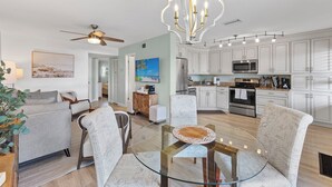 A modern living room with a glass coffee table, a ceiling fan, and a dining area with chairs.