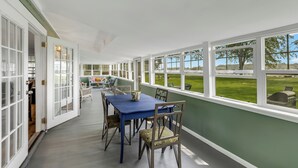 Une véranda avec une table et des chaises bleues, donnant sur une pelouse, et une porte menant à un espace intérieur.