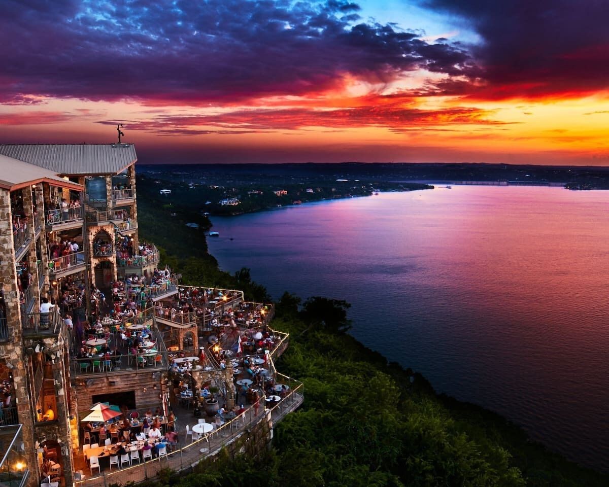 Ein mehrstöckiges Gebäude mit Außenbereich, der auf ein Gewässer blickt, mit einem auffälligen Balkon und Blick auf den Sonnenuntergang.