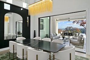 Uma sala de jantar moderna com uma mesa preta, cadeiras brancas, um espelho grande e vista para o exterior.