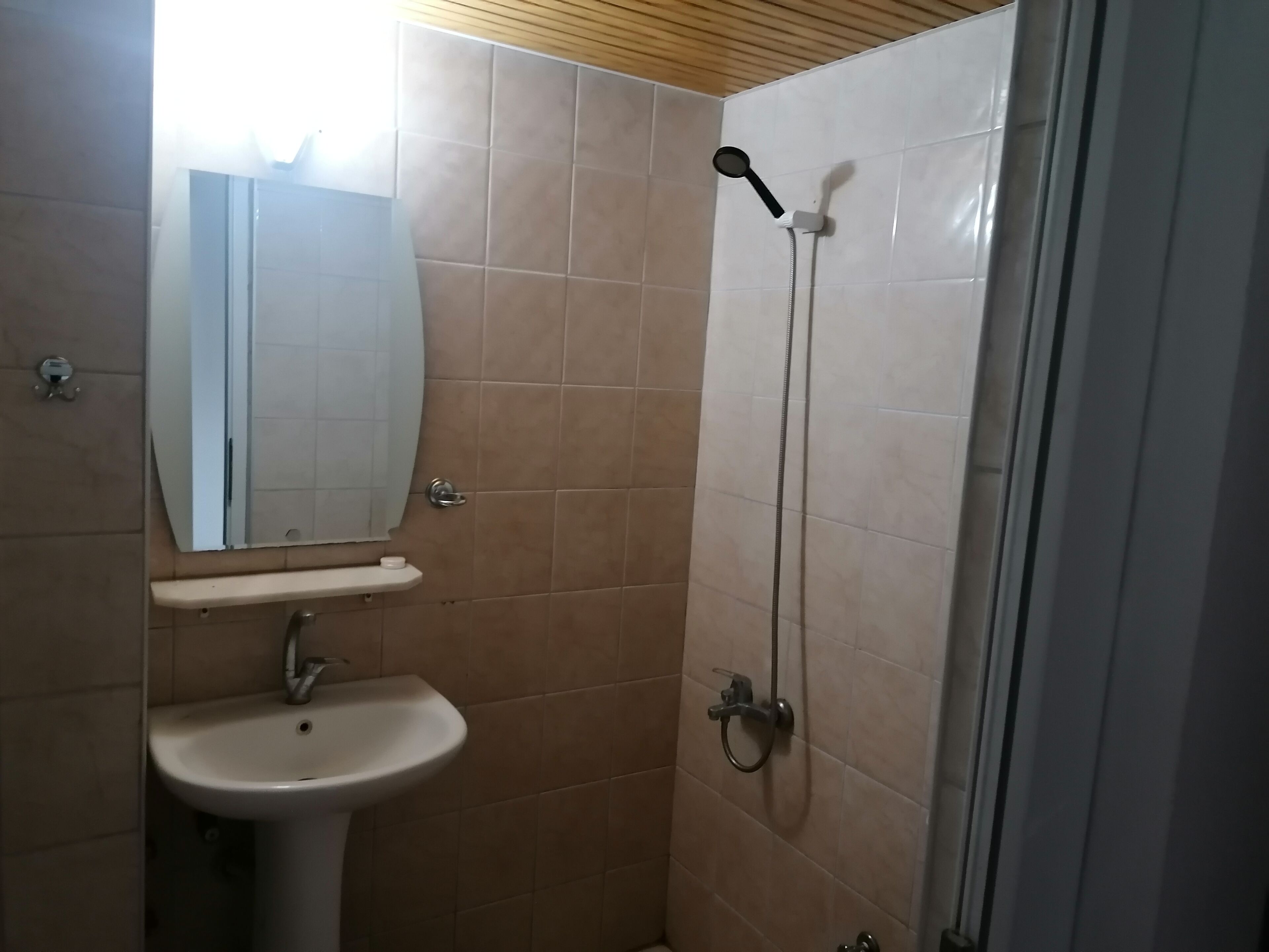 Casa de banho com lavatório, espelho e chuveiro.