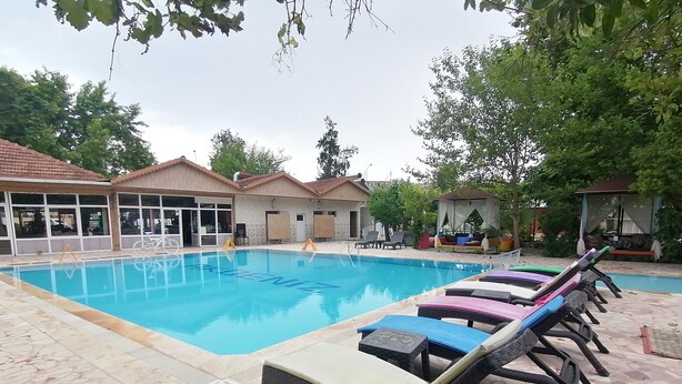 A swimming pool with lounge chairs and a building with large windows in the background. - Pasa Restaurant & Pansiyon (Kemer)