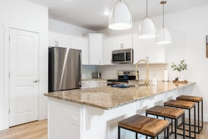 A modern kitchen with white cabinets, stainless steel appliances, granite countertops, and wooden stools. - Fishing Dock & Lake Taneycomo Views, Near Branson Landing with Free Tickets (Branson)