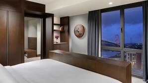 Habitación de hotel moderna con una cama grande, un escritorio de madera, vistas a un puente y un elemento decorativo en la pared.