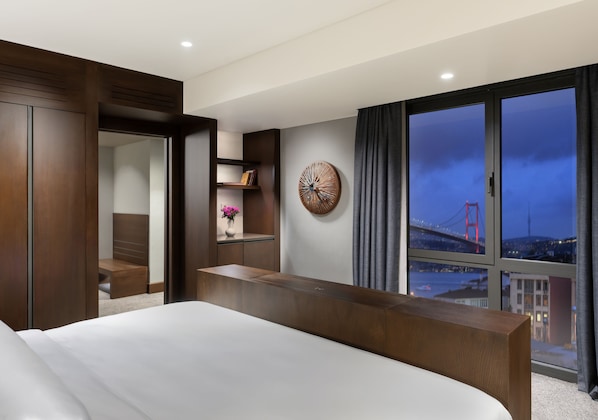 Een moderne hotelkamer met een groot bed, een houten bureau, uitzicht op een brug en een decoratief kunstwerk aan de muur.