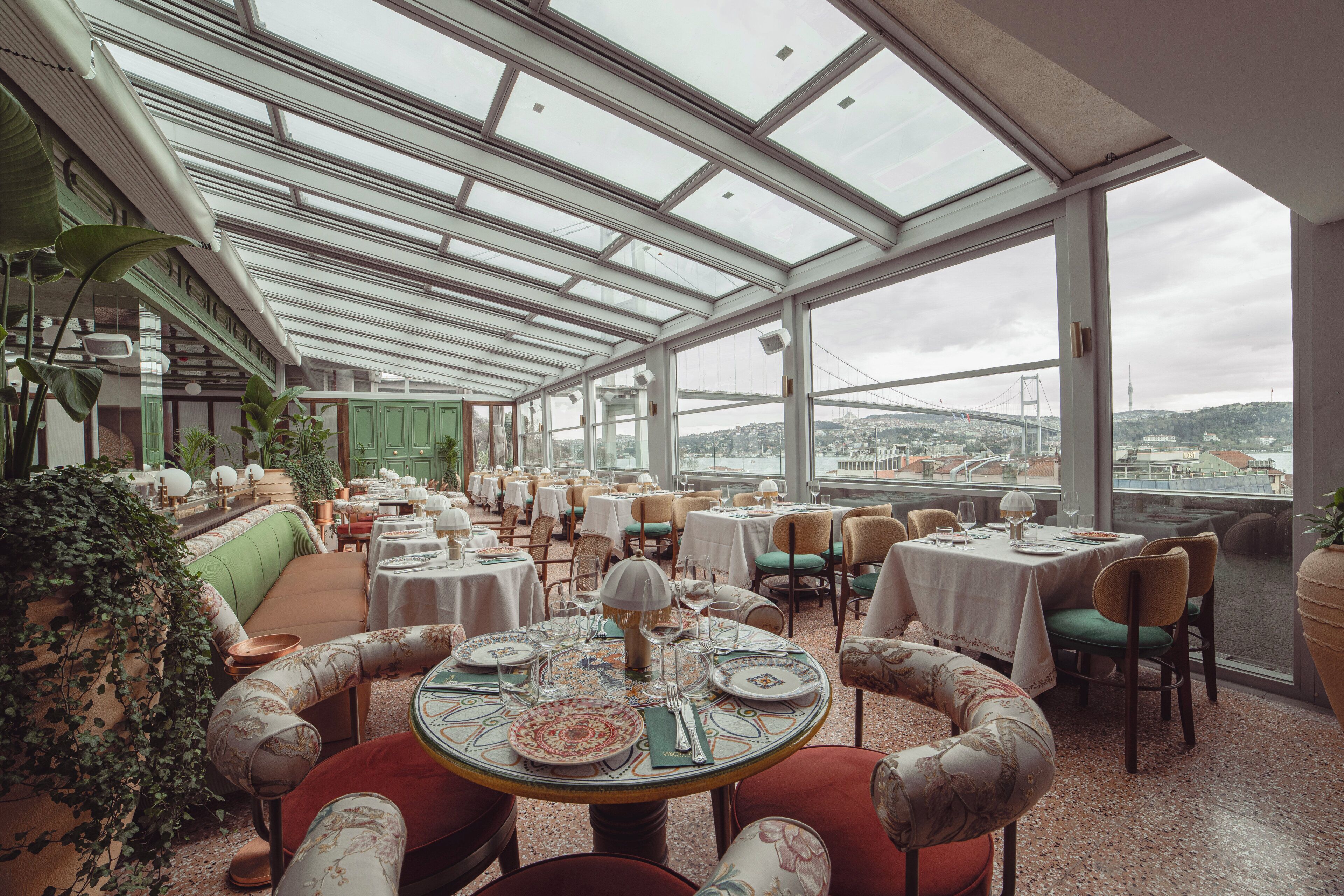 A restaurant with a high ceiling and large windows, offering views of a bridge and cityscape.