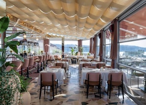 Un restaurante con mesas dispuestas para comer, amplios ventanales que ofrecen vistas y un techo con diseño ondulado.
