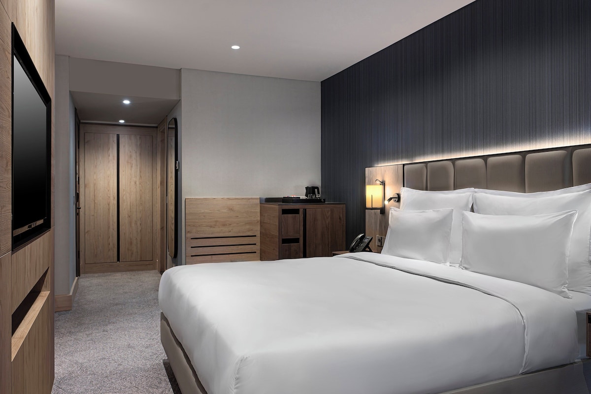 Een hotelkamer met een groot bed, een televisie, een bureau met een lamp en een kledingkast.
