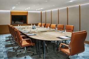 A conference room with a long table, brown leather chairs, and a large screen.