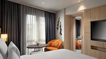 Una habitación de hotel con una cama, una mesa redonda, una silla, un televisor y vistas al exterior a través de amplios ventanales.