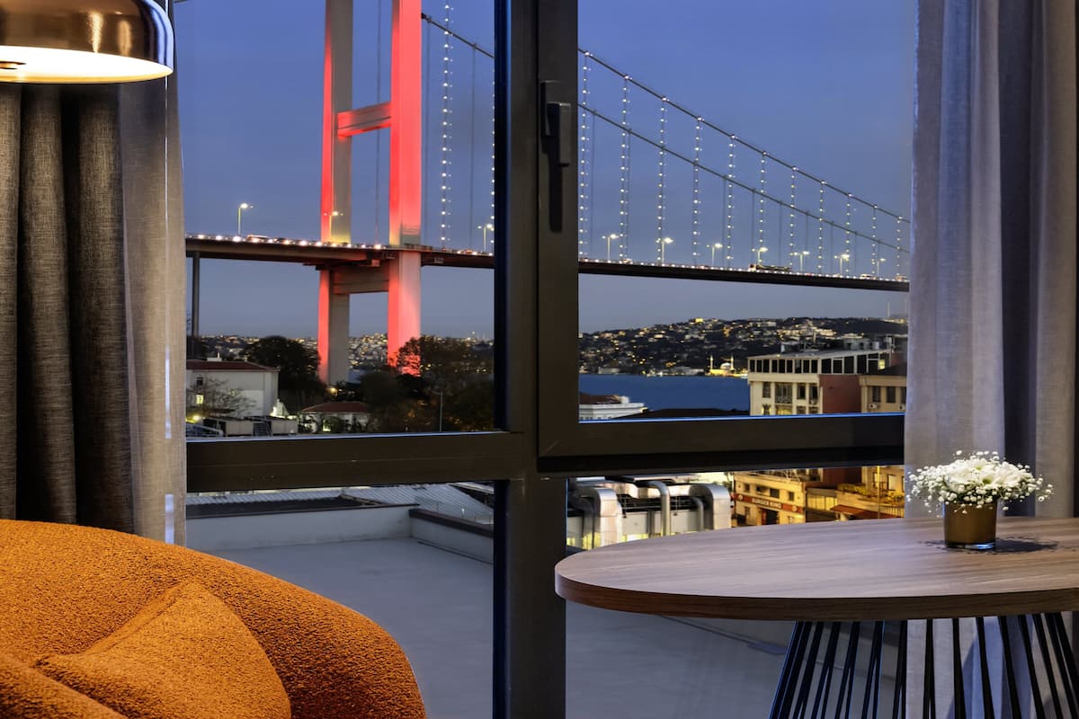 Une chambre d’hôtel moderne dotée d’une grande fenêtre donnant sur un pont et sur le paysage urbain.