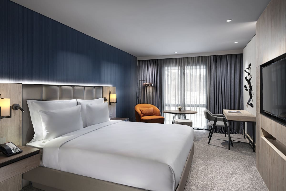 Une chambre d’hôtel avec un grand lit, un bureau, une chaise, une télévision et une lampe.