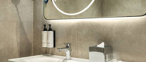 A modern bathroom with a large mirror, a white sink, and a towel rack.