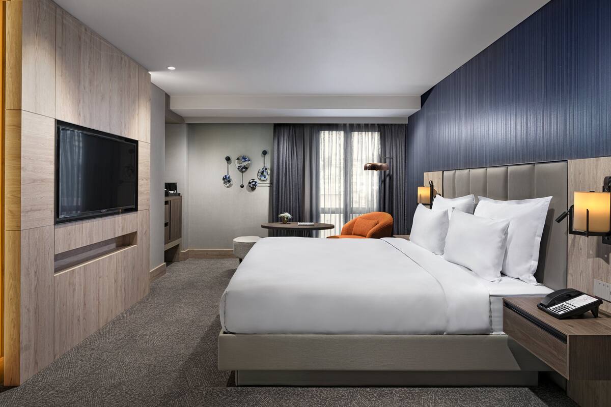 Une chambre d’hôtel moderne dotée d’un grand lit, d’un téléviseur à écran plat, d’un bureau avec un téléphone et d’une petite table avec une lampe.