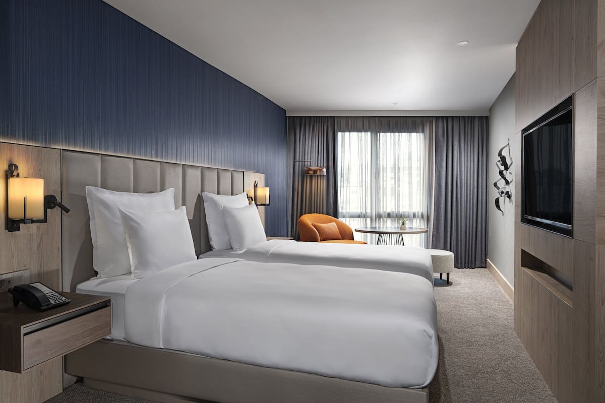Une chambre d’hôtel avec deux lits, une télévision, un bureau avec un téléphone et une chaise.