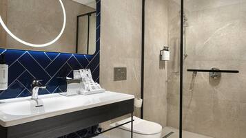 A modern bathroom with a glass-enclosed shower, a white sink with a black faucet, and a mirror with a circular light.