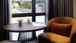 Una habitación con vista a un puente, una mesa con una taza y un libro, y una silla marrón.