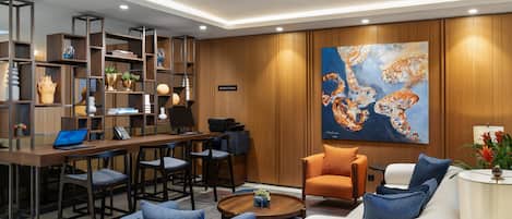 A modern hotel lobby with a wooden reception desk, seating area, and a large abstract painting on the wall.