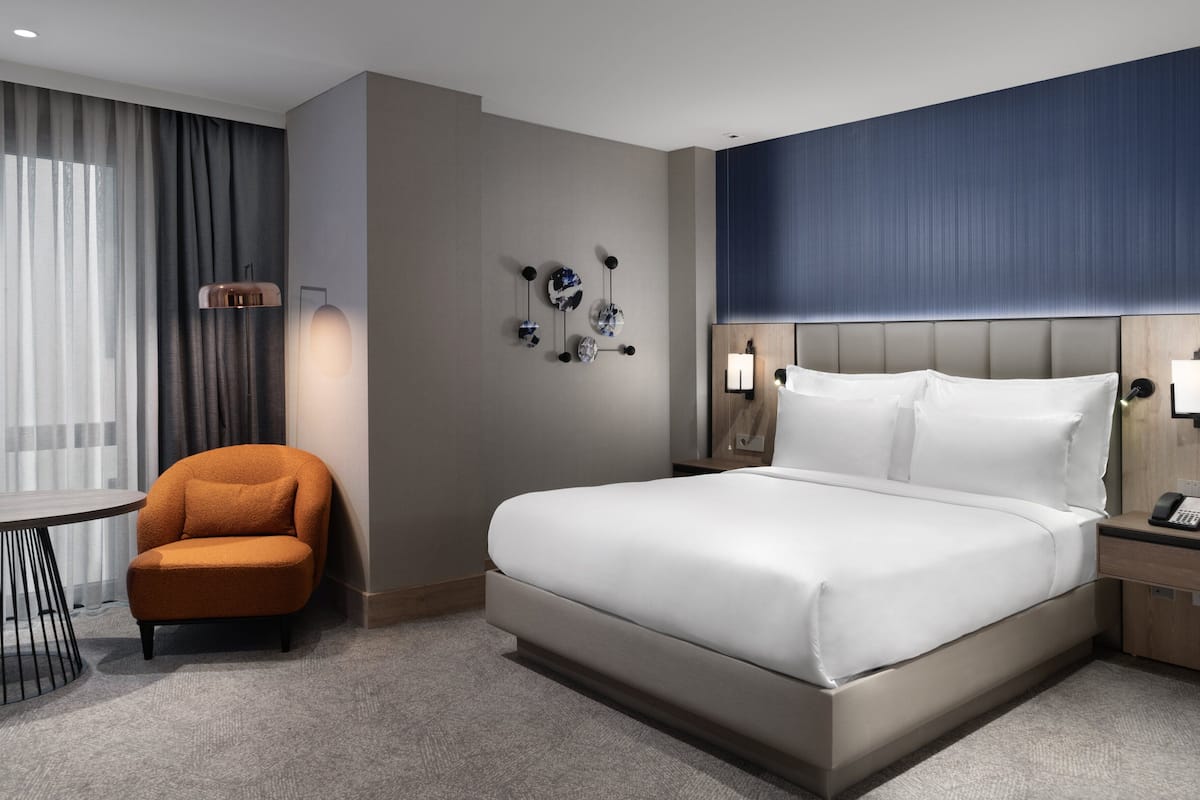 Une chambre d’hôtel avec un grand lit, une table de chevet avec un téléphone, une chaise, une table et un luminaire fixé au mur.