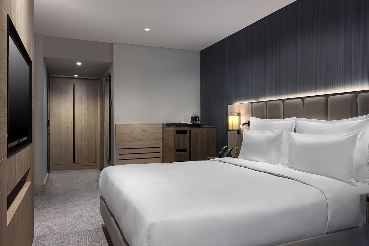 Une chambre d’hôtel moderne dotée d’un grand lit, d’un téléviseur à écran plat, d’une armoire en bois et d’un bureau avec une lampe.