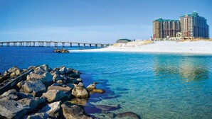 Ein Hotel an der Küste mit einem Steg, der ins Wasser ragt, einem Sandstrand und einem strahlend blauen Himmel.