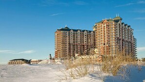 Ein Hochhaus-Hotel mit mehreren Etagen, gelegen an einem sandigen Strand mit spärlicher Vegetation.