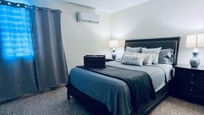 Ein modernes Hotelzimmer mit einem Bett, zwei Nachttischlampen, einem kleinen Nachttisch und einem Fenster mit Vorhängen.
