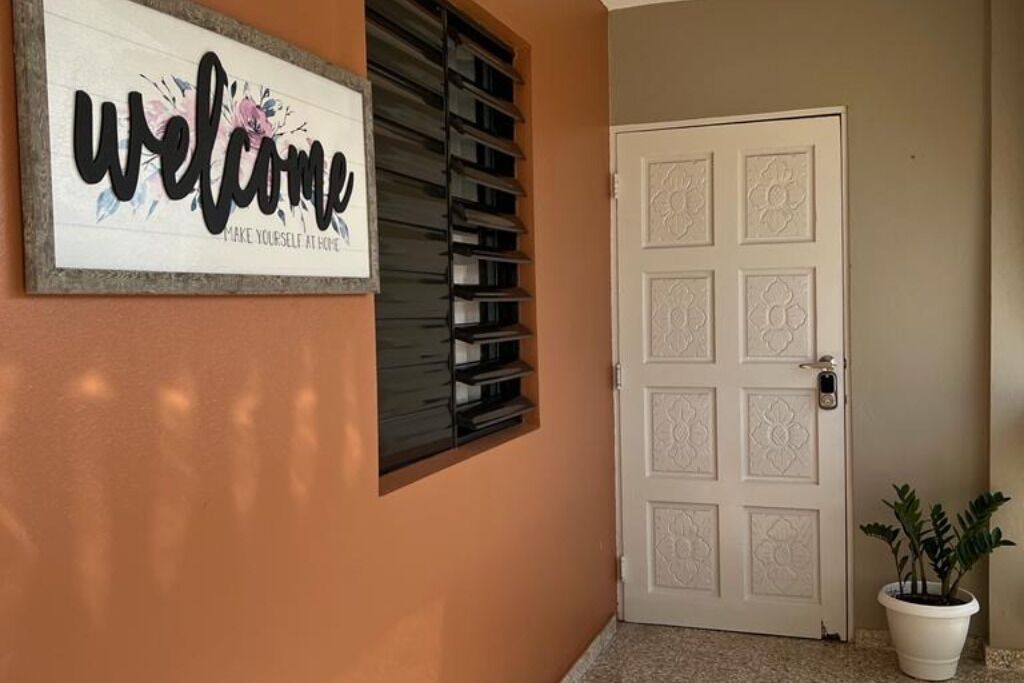 A welcome sign with floral design, a white door with decorative panels, and a potted plant beside the door.