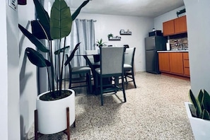 A compact living space with a dining area, kitchen, and potted plants.