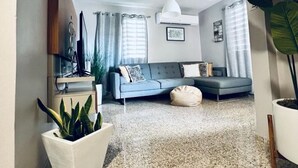 Ein modernes Wohnzimmer mit einem grauen Sofa, einem weißen Couchtisch und einer großen Kübelpflanze.