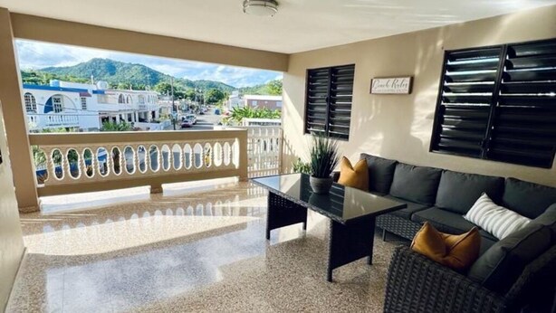 Ein Balkon mit Blick auf Gebäude und Berge, eine Couch, ein Couchtisch und ein Blumentopf.