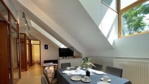 Un comedor con una mesa preparada para cuatro personas, un televisor sobre la mesa y un ventanal que deja entrar abundante luz natural.