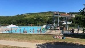Un parque acuático con una piscina grande, un tobogán de agua y un área de césped donde la gente descansa.