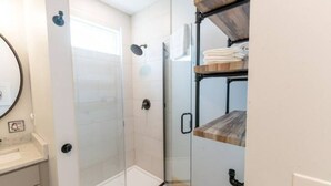 Ein modernes Badezimmer mit Duschabtrennung aus Glas, einem Holzboden mit Handtüchern und einem weißen Waschbecken.