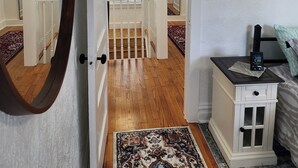 A bedroom with a wooden floor, a nightstand with a clock, a bed with patterned bedding, a large mirror, and a window with blinds. - Great for working professionals: medical, construction, etc. LTE, or Mid-term! (Grand Rapids)