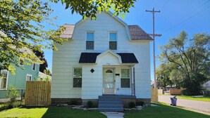 A two-story house with a front porch, a small front yard, and a sidewalk leading to the entrance. - Great for working professionals: medical, construction, etc. LTE, or Mid-term! (Grand Rapids)