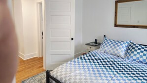 A bedroom with a checkered bedspread, a white door, a nightstand with a clock, and a mirror on the wall. - Great for working professionals: medical, construction, etc. LTE, or Mid-term! (Grand Rapids)