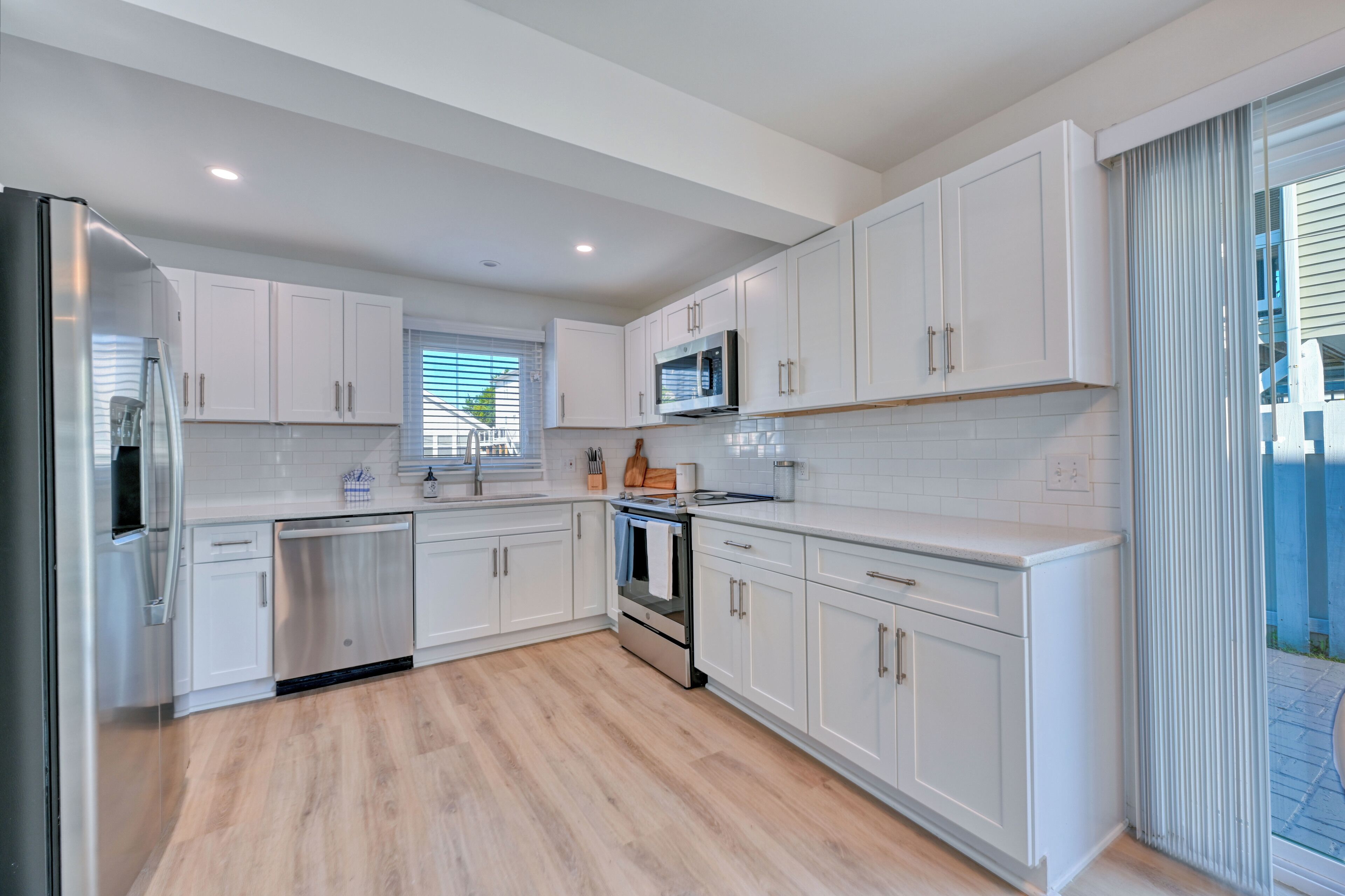 A modern kitchen with white cabinets, stainless steel appliances, and a wooden floor.
