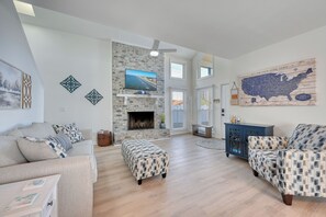 A spacious living room with a stone fireplace, a mounted TV, and a large map of the U.S. on the wall. - Private Home - 1 Block to ocean- Private Fenced in Yard - Pet Friendly (North Myrtle Beach)