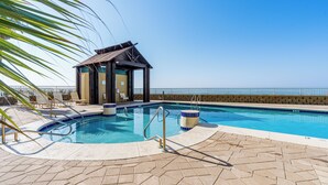 Una piscina con bordo in legno, poltrona relax e vista sull'oceano.