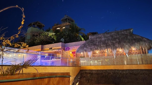 A resort with a thatched-roof structure, a glass pool, and a night sky. - Casa Pepe Hostel Boutique - Sayulita (Sayulita)