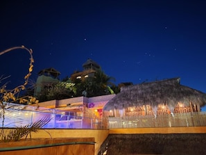 A resort with a thatched-roof structure, a glass pool, and a night sky. - Casa Pepe Hostel Boutique - Sayulita (Sayulita)